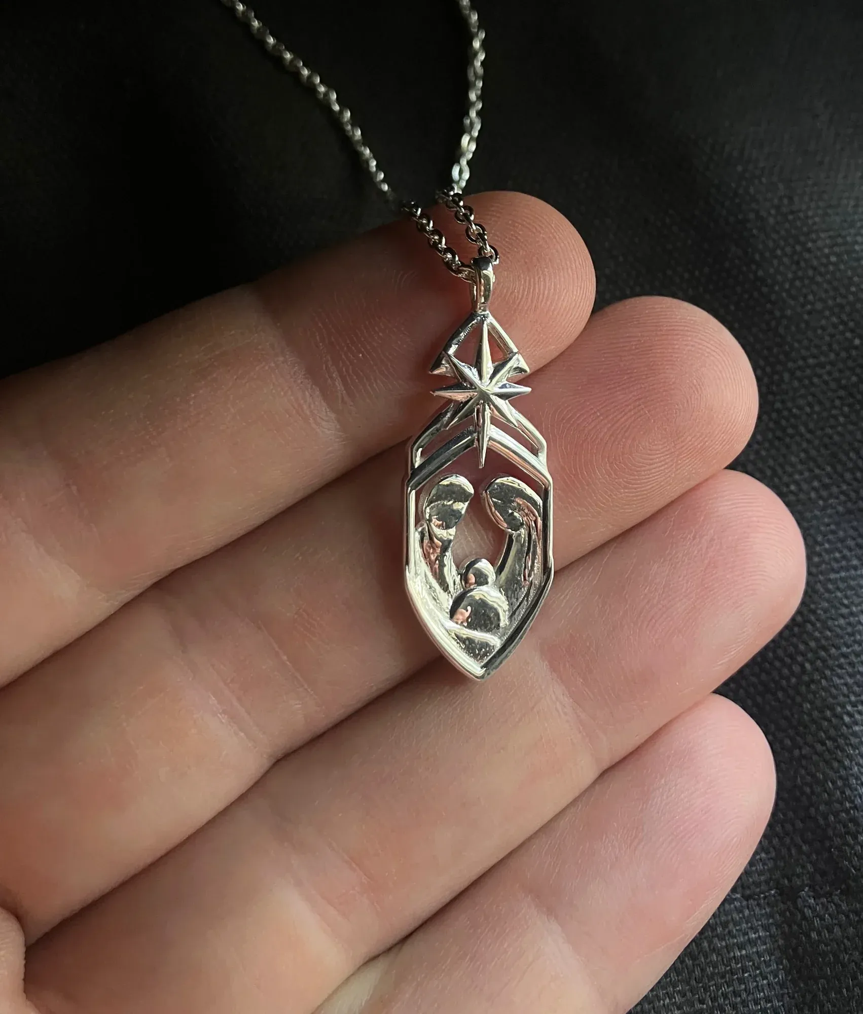 The pendant held across four fingertips, showing its scale and the open bridged spaces around the star.