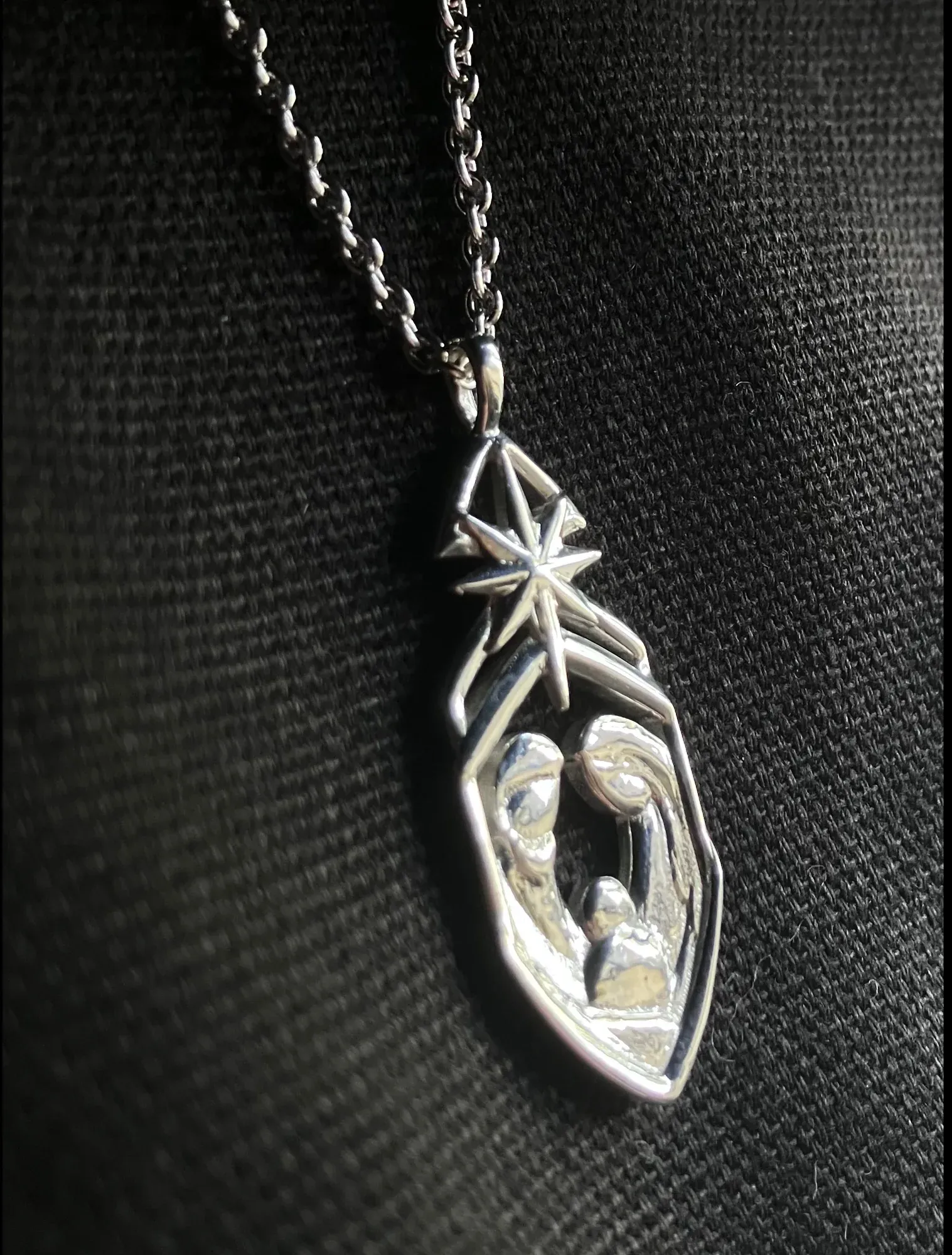 The pendant worn against a black knit, raking light picking out the star's facets and the figures inside the frame.