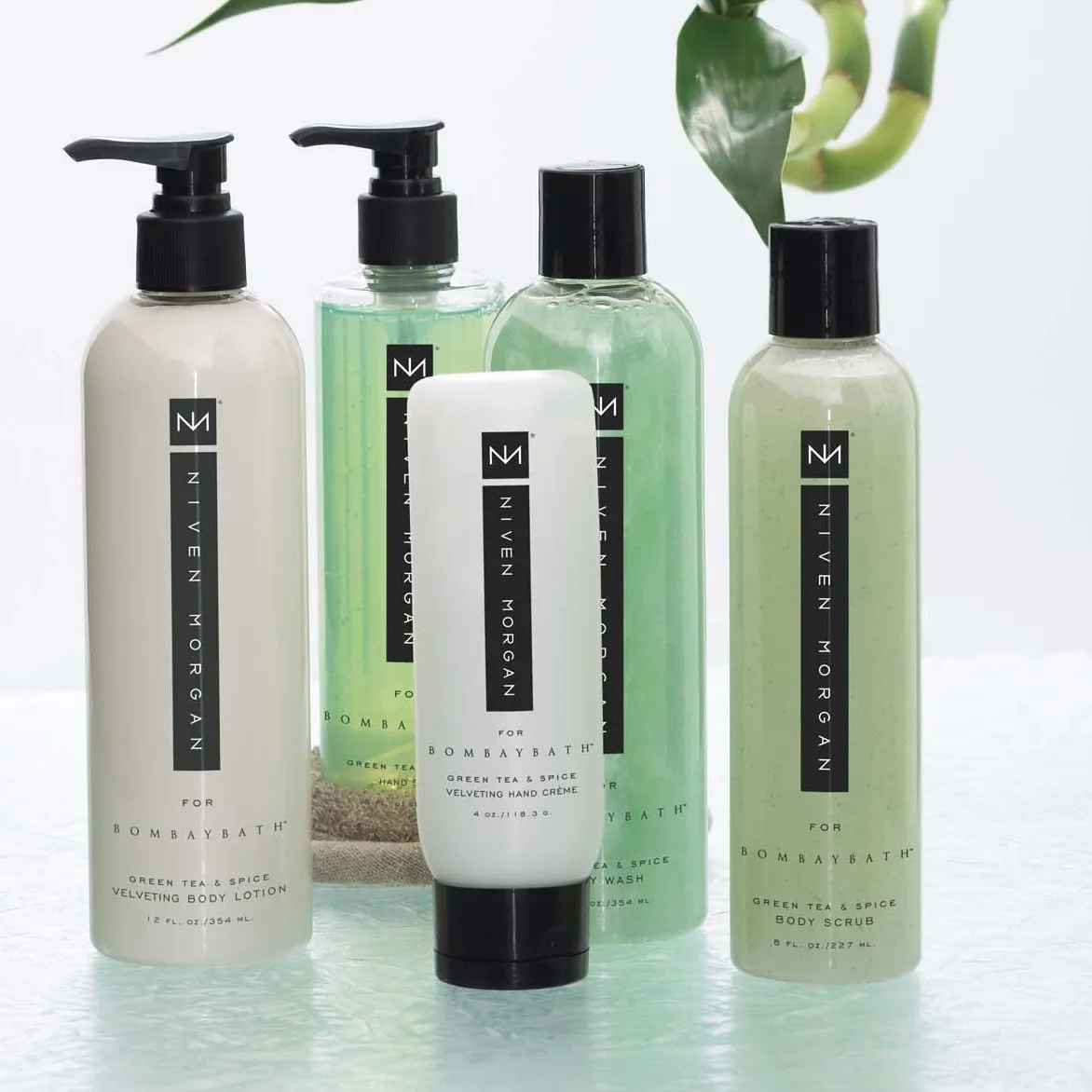 The green tea and spice group in soft greens, arranged on a glass shelf with lucky bamboo behind.